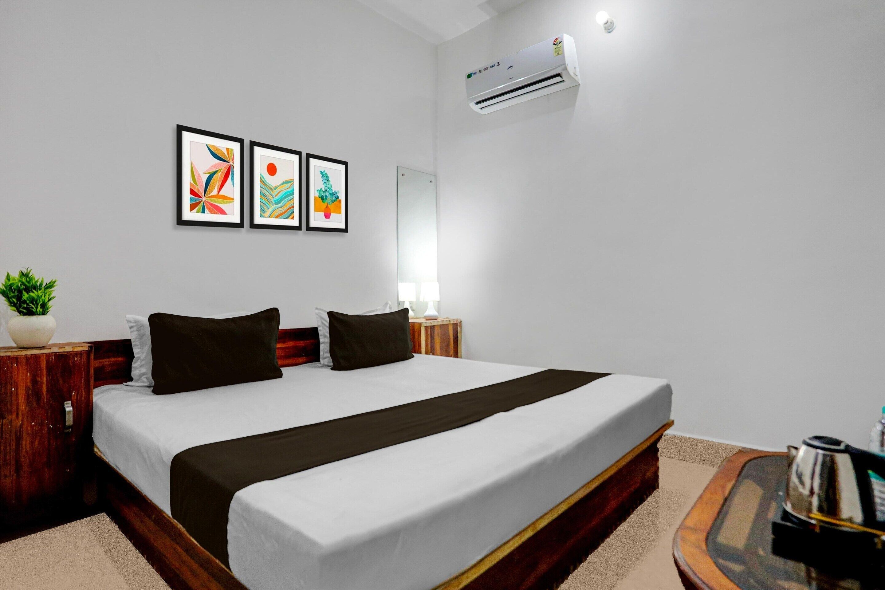 Une chambre d’hôtel comprenant un lit, des tables de chevet, une plante en pot, des œuvres d’art, un appareil de climatisation et un miroir.