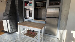 Eine Küche mit Einbauofen, Mikrowelle und Kühlschrank, einem Holztisch, gemusterten Bodenfliesen und einer Ziegelwand.