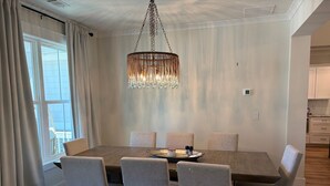 Un comedor con una mesa de madera, seis sillas, una araña y vistas a través de un ventanal.