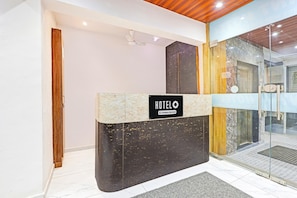 A hotel reception desk with a 'HOTELO' sign, a wooden door, and a glass entrance leading to a bathroom.