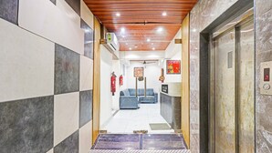 Um saguão de hotel com piso xadrez, balcão de recepção, sofá azul e um elevador.
