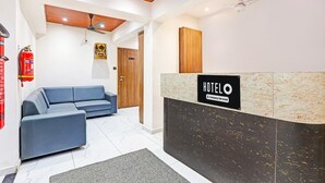 Uma área de recepção de hotel, com balcão de atendimento, sofá azul, teto de madeira e extintor de incêndio.
