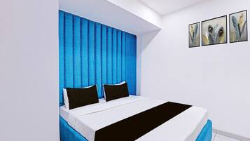Un dormitorio con cama, cabecera azul, paredes blancas y tres cuadros enmarcados.