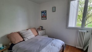 Une chambre à coucher comprenant un lit, une table de chevet, une commode, un radiateur, une fenêtre et un tapis.