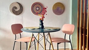 A round table with a vase of flowers, two chairs, and six woven wall hangings. - Jozi Muse: Retro Oasis in the Heart of Sandton (Sandton)