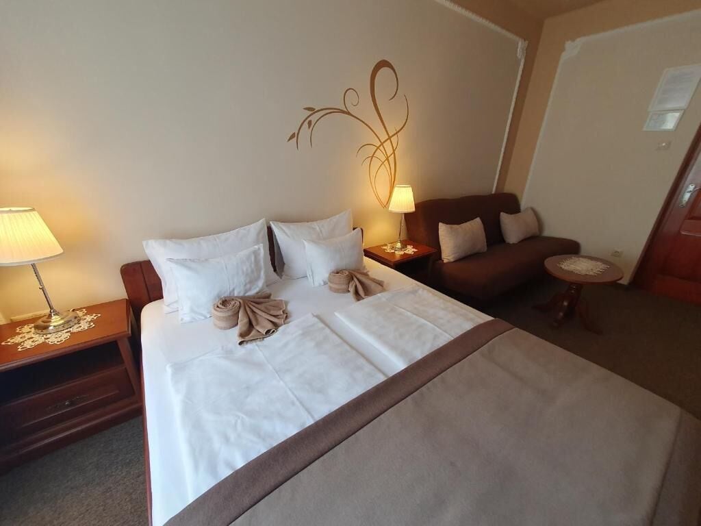 Una habitación de hotel con una cama, dos mesitas de noche, una lámpara, un adorno en la pared, un sofá y una pequeña mesa redonda.