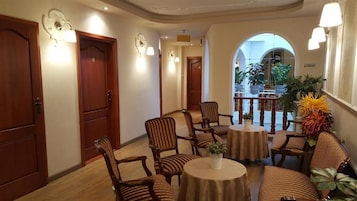 A hotel lobby with wooden doors, striped chairs, round tables, and a view of the outdoors through an arched window.