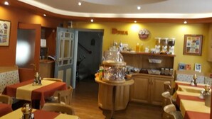 Un ristorante con tavoli rivestiti da tovaglie rosse e gialle, un bancone con una vetrina e un cartello che riporta la scritta 'DUNA'.
