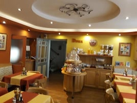 Restaurante com mesas cobertas por toalhas vermelhas e amarelas, um balcão com vitrine de vidro e uma placa com o nome 'DUNA'.