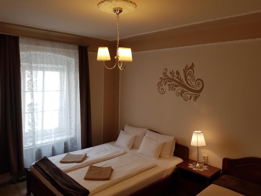 Habitación de hotel con cama doble, mesita de noche con lámpara, un adorno en la pared y una ventana con cortinas.