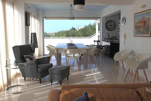 Ein modernes Wohnzimmer mit einer Couch, einem Esstisch, Stühlen, einem Balkon mit Blick und einer Küchenzeile.