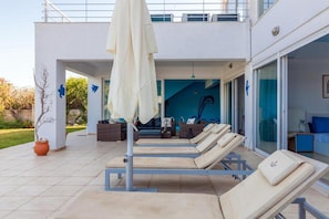 Eine moderne Lounge-Bereich im Freien mit Liegestühlen, einem weißen Sonnenschirm und einer Sitzgelegenheit am Pool.