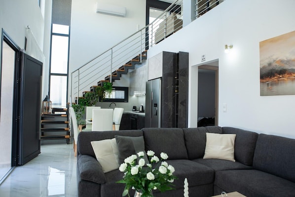 Ein modernes Wohnzimmer mit grauem Sofa, einer Treppe, einer Küche und einem Essbereich.