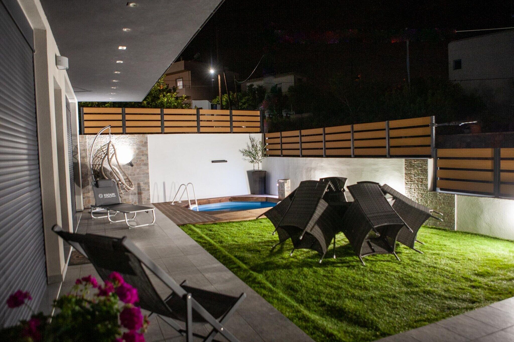 Une terrasse extérieure moderne, dotée d’une piscine, de chaises longues et d’une pelouse bien entretenue.