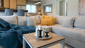 Een moderne woonkamer met een bank, een bijzettafeltje met kaarsen, en een keuken op de achtergrond.