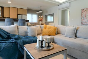Ein modernes Wohnzimmer mit einer Couch, einem Couchtisch mit Kerzen und einer Küche im Hintergrund.
