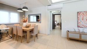 Een moderne eetruimte met een tafel, stoelen, een kinderstoel, hanglampen, een spiegel en een decoratieve vaas.