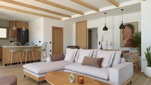 Un soggiorno moderno con un divano componibile, travi in legno, lampade a sospensione e una zona pranzo con sgabelli da bar.