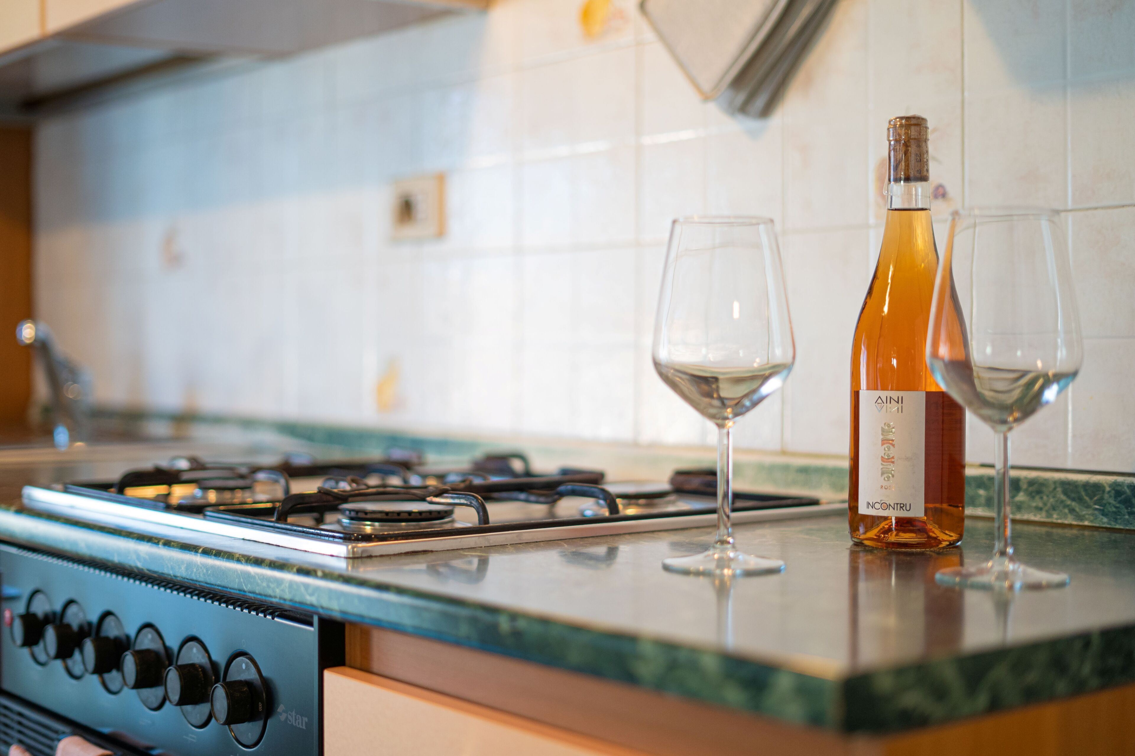 Een keuken met een gasfornuis, twee wijnglazen en een fles wijn op het aanrecht.