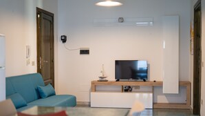 Uma sala de estar com um sofá azul, uma televisão sobre um suporte de madeira, uma miniatura de navio e um armário branco.
