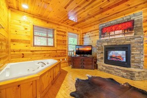 A log cabin interior with a stone fireplace, a television, and a large bathtub. - *Relaxing 5BD Lodge w/ VIEWS | Games + Hot Tub* (Sevierville)