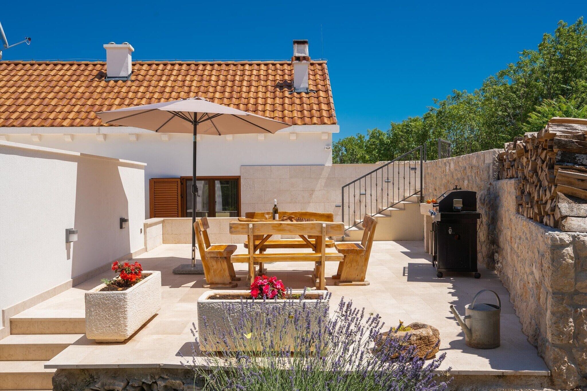 Une terrasse avec une table et des chaises, un barbecue et un mur en pierre.