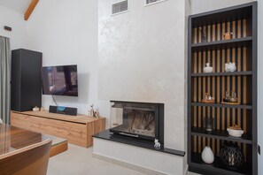 Ein modernes Wohnzimmer mit Flachbildfernseher, Kamin, Holzschrank und einer schwarzen Regaleinheit mit Dekorationselementen.