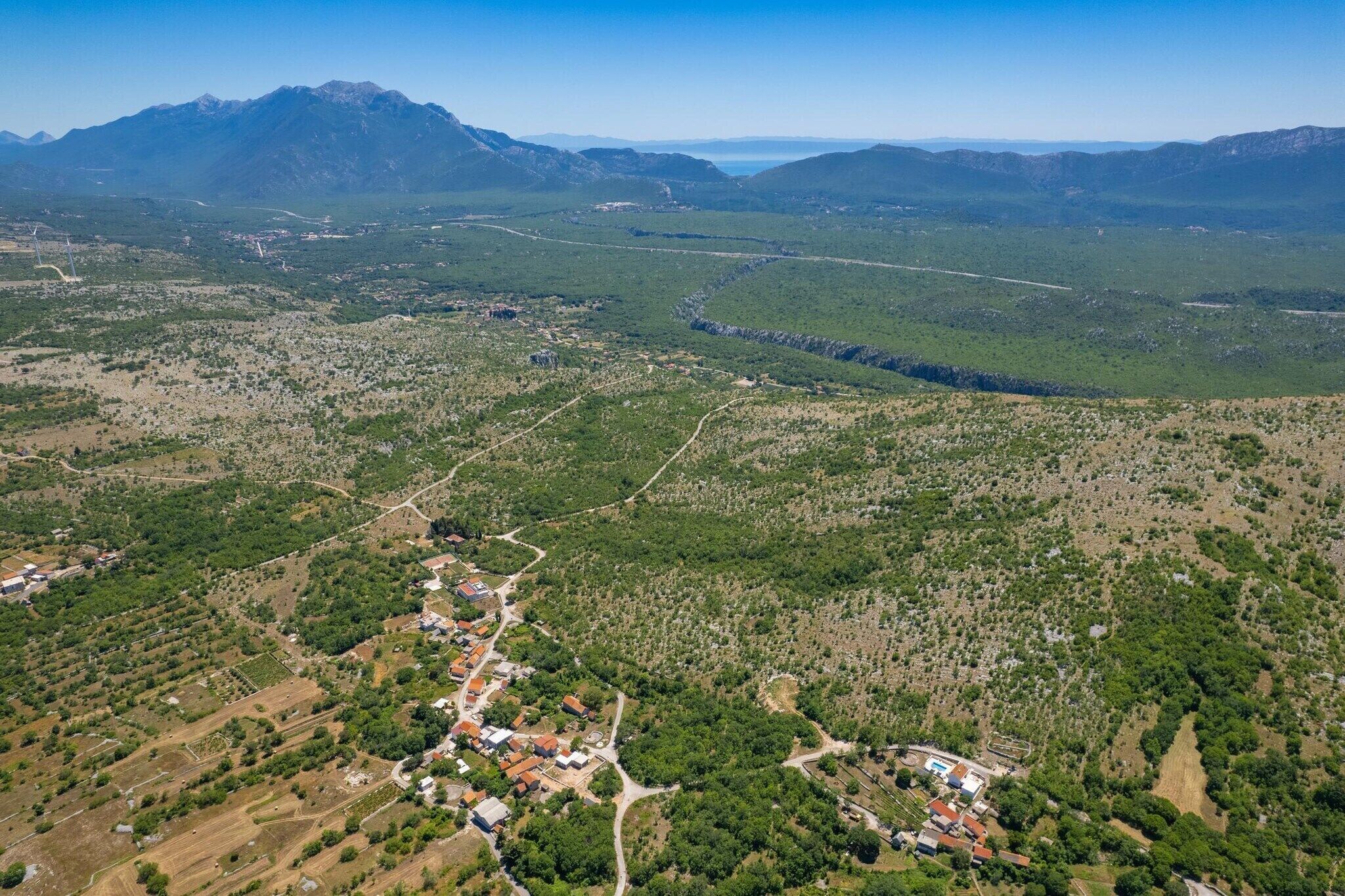 Ett flygbildsbild av en stad med en huvudgata, omgivande grönska och berg i fjärran.