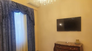A room with a flat-screen TV mounted on the wall, a wooden dresser with drawers, and a window with blue curtains. - Impero Vaticano Ottaviano Apartment  (Rome)