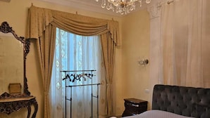 A bedroom with a large bed, a chandelier, a mirror, and a window with curtains. - Impero Vaticano Ottaviano Apartment  (Rome)