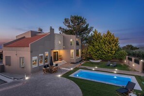 A modern house with a swimming pool, outdoor seating, and a large tree. - 10-Guest Countryside Villa with Barbecue (Heraklion)