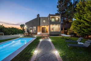 Une maison moderne à deux étages, dotée d’une piscine, d’un espace salon extérieur et d’une pelouse bien entretenue.