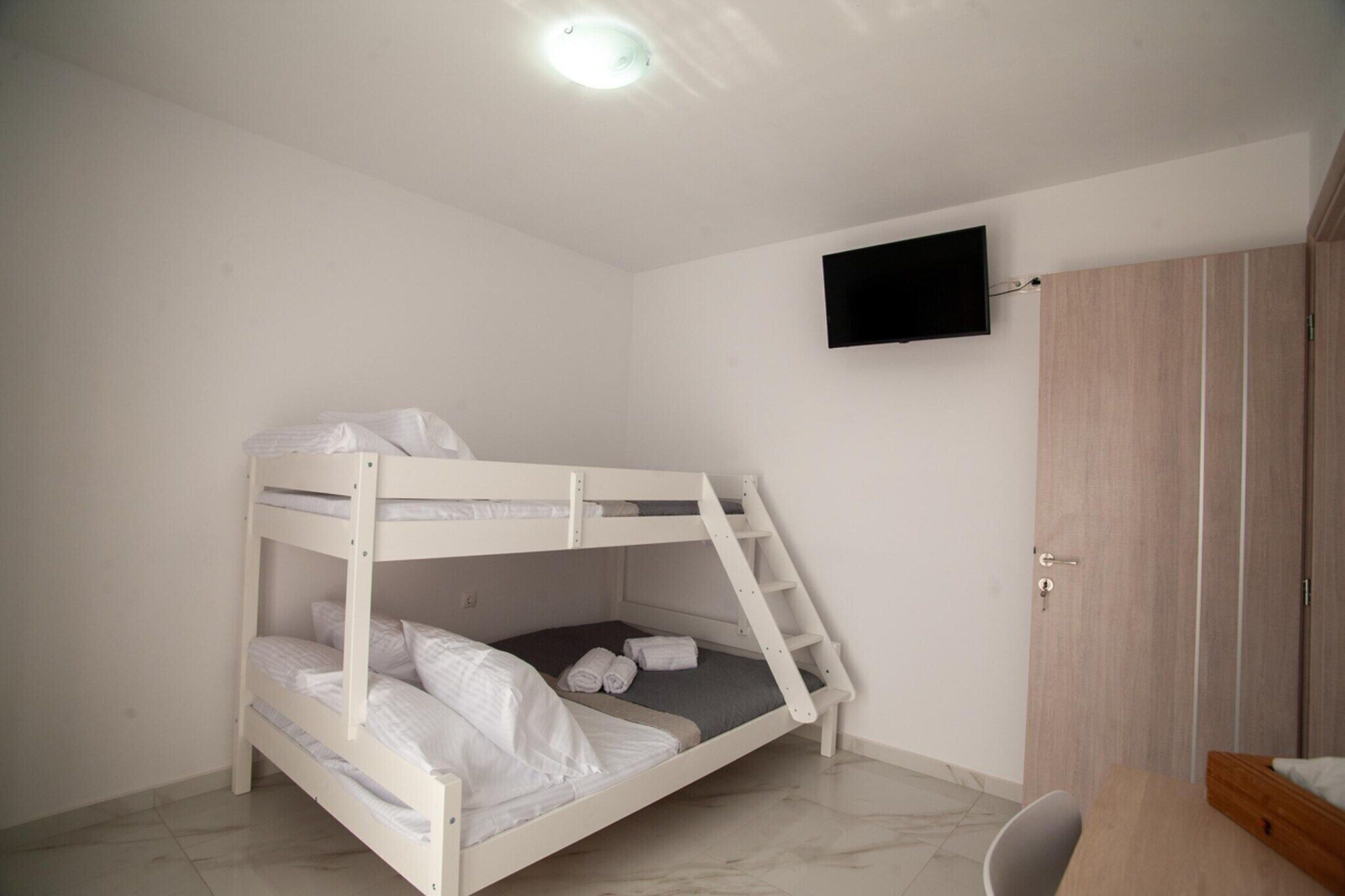 A bunk bed with a TV mounted on the wall, a wooden wardrobe, and a desk with a chair.