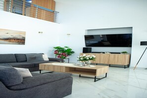 A modern living room with a sofa, coffee table, TV, and a plant. - Modern Villa Vacation for 6 with Pool (Gouves)