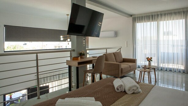 Ein Hotelzimmer mit Bett, einer Couch, einem an der Wand befestigten Fernseher, einem kleinen Tisch und einem Balkon mit Geländer.