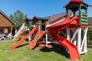 A playground with a slide and climbing area, surrounded by wooden playhouses.
