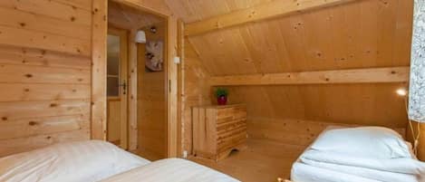 A wooden cabin room with two beds, a dresser, and a door leading to another room.