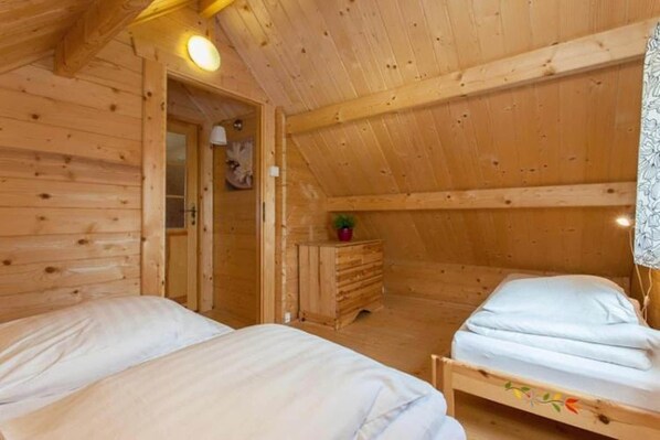 A wooden cabin room with two beds, a dresser, and a door leading to another room.