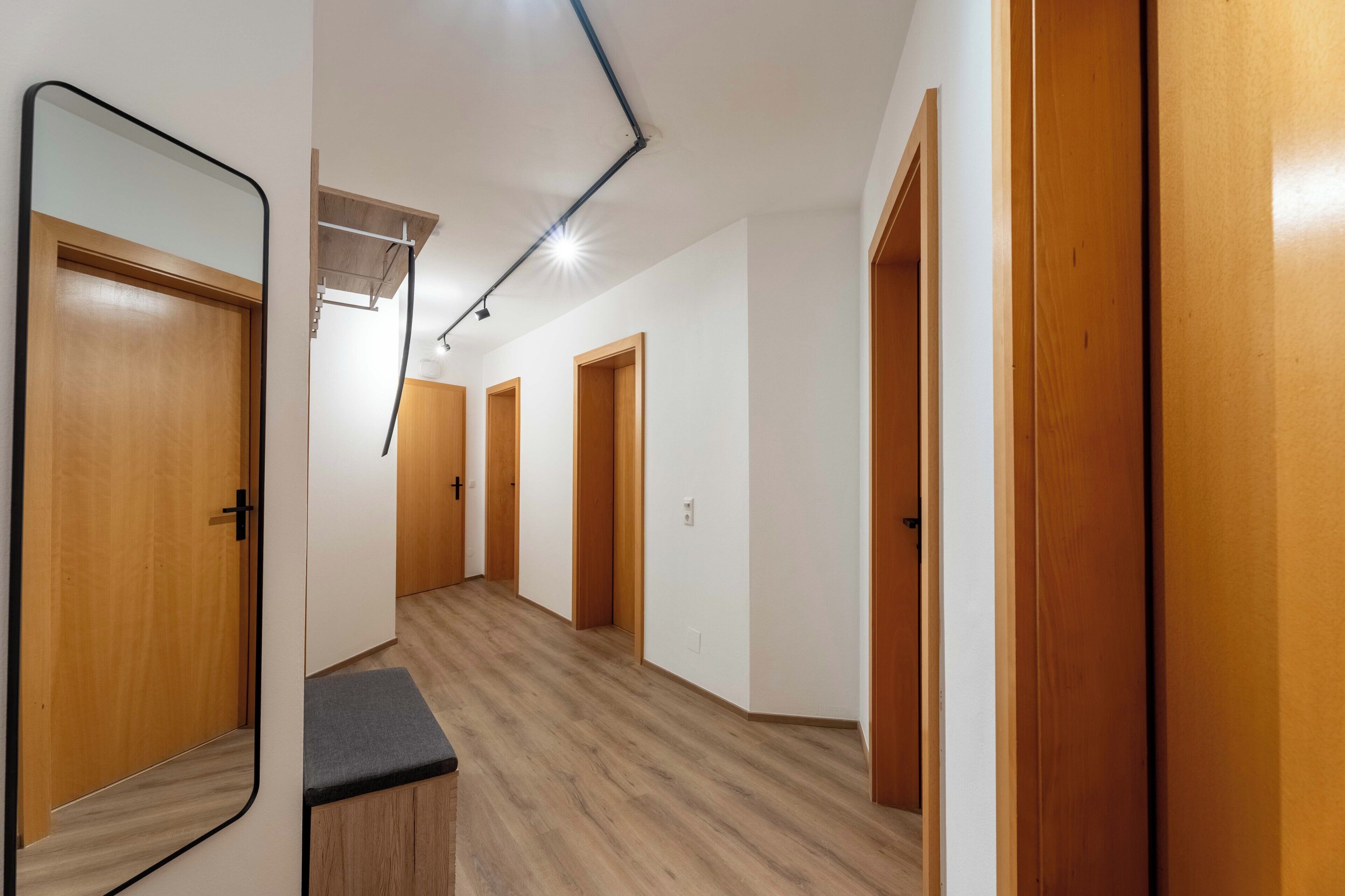 A hallway with wooden doors, a bench, and a ceiling light fixture.