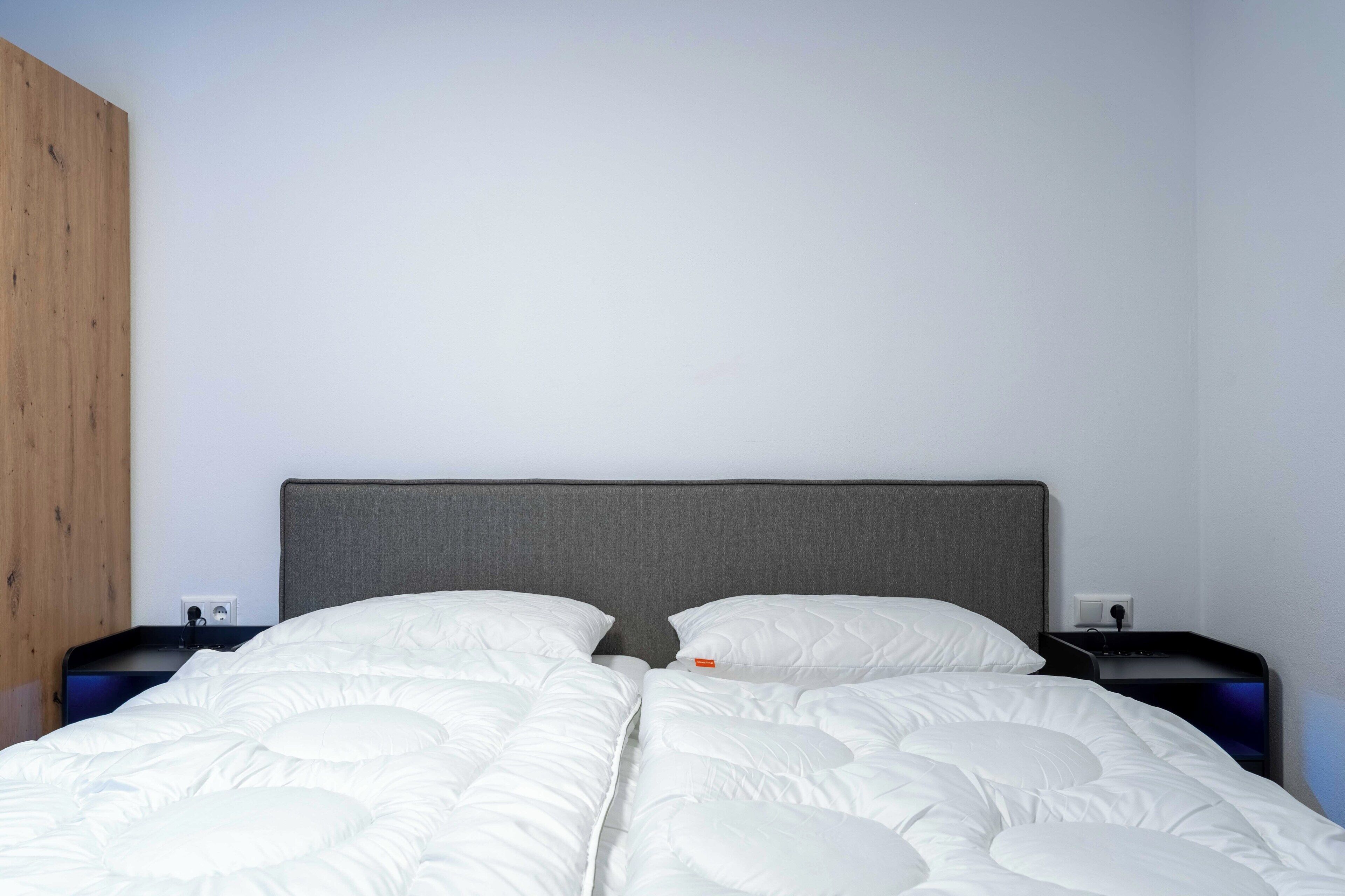 A bed with white bedding, a grey headboard, and a wooden panel on the left.