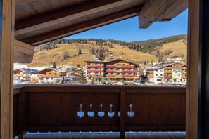 Un balcon en bois offrant une vue sur un village de montagne, avec des bâtiments dotés de balcons et un paysage enneigé.
