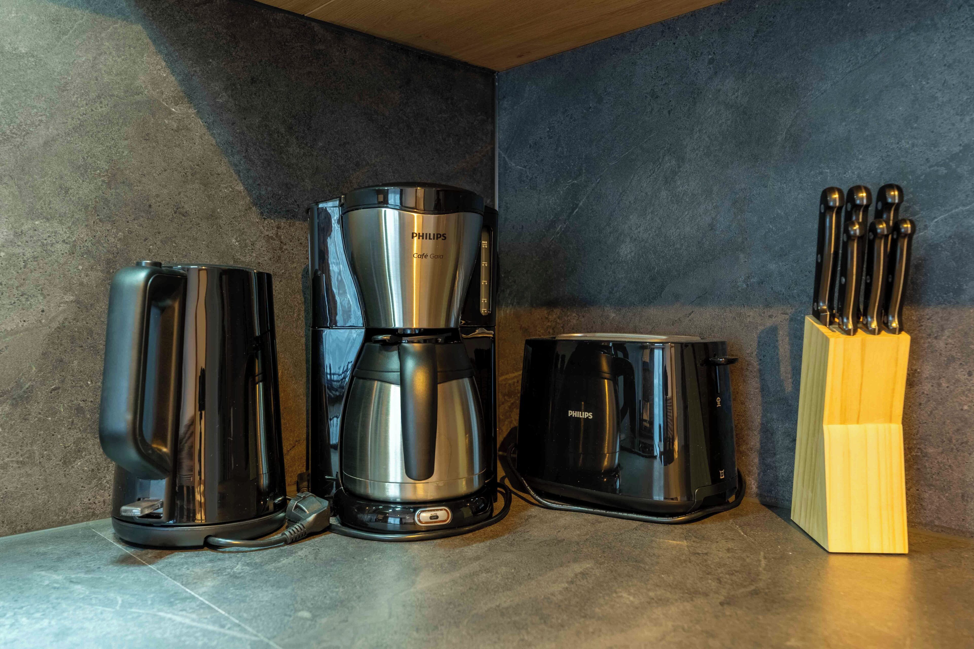 A kitchen with a coffee maker, a kettle, and a toaster.