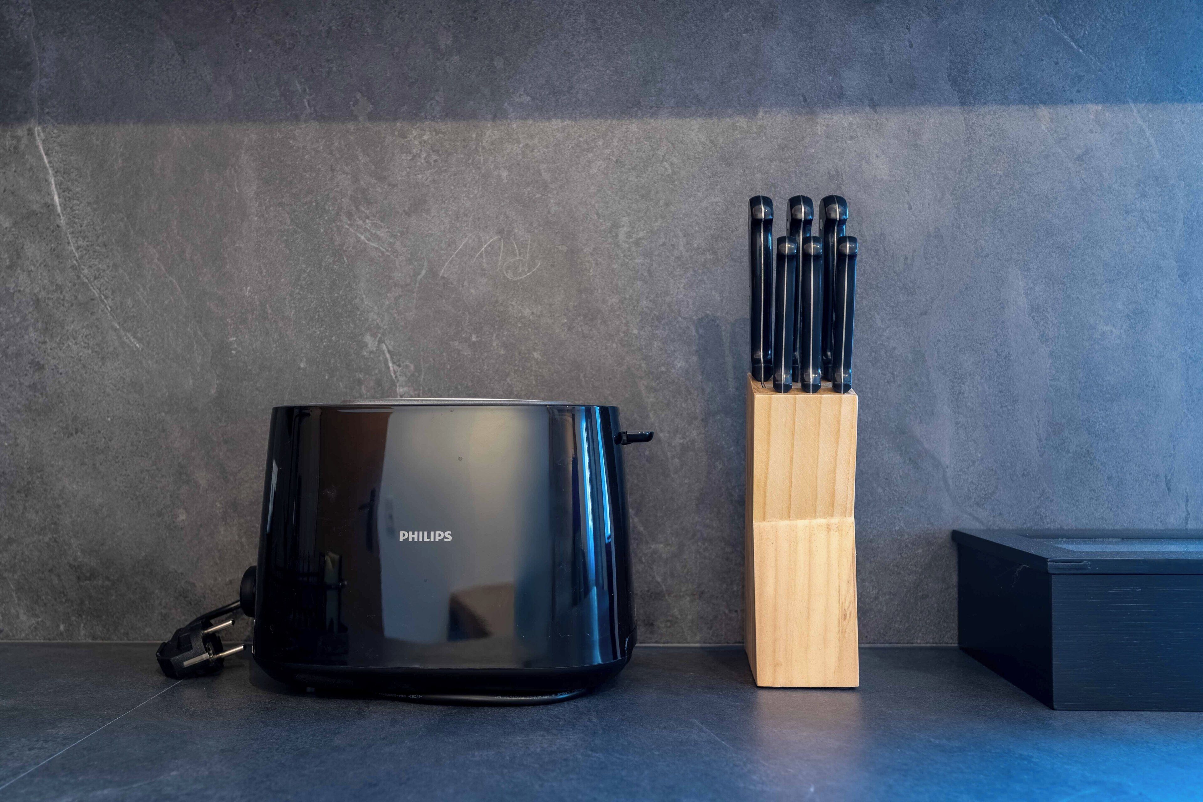 Um aparelho Philips preto, um suporte de utensílios de madeira e uma caixa preta em uma bancada.