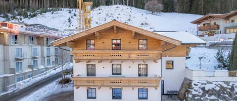 A multi-story wooden building with balconies, a ski lift in the background, and a snowy landscape.
