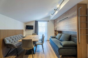 A modern living room with a wooden dining table, a tufted sofa, and a built-in TV.
