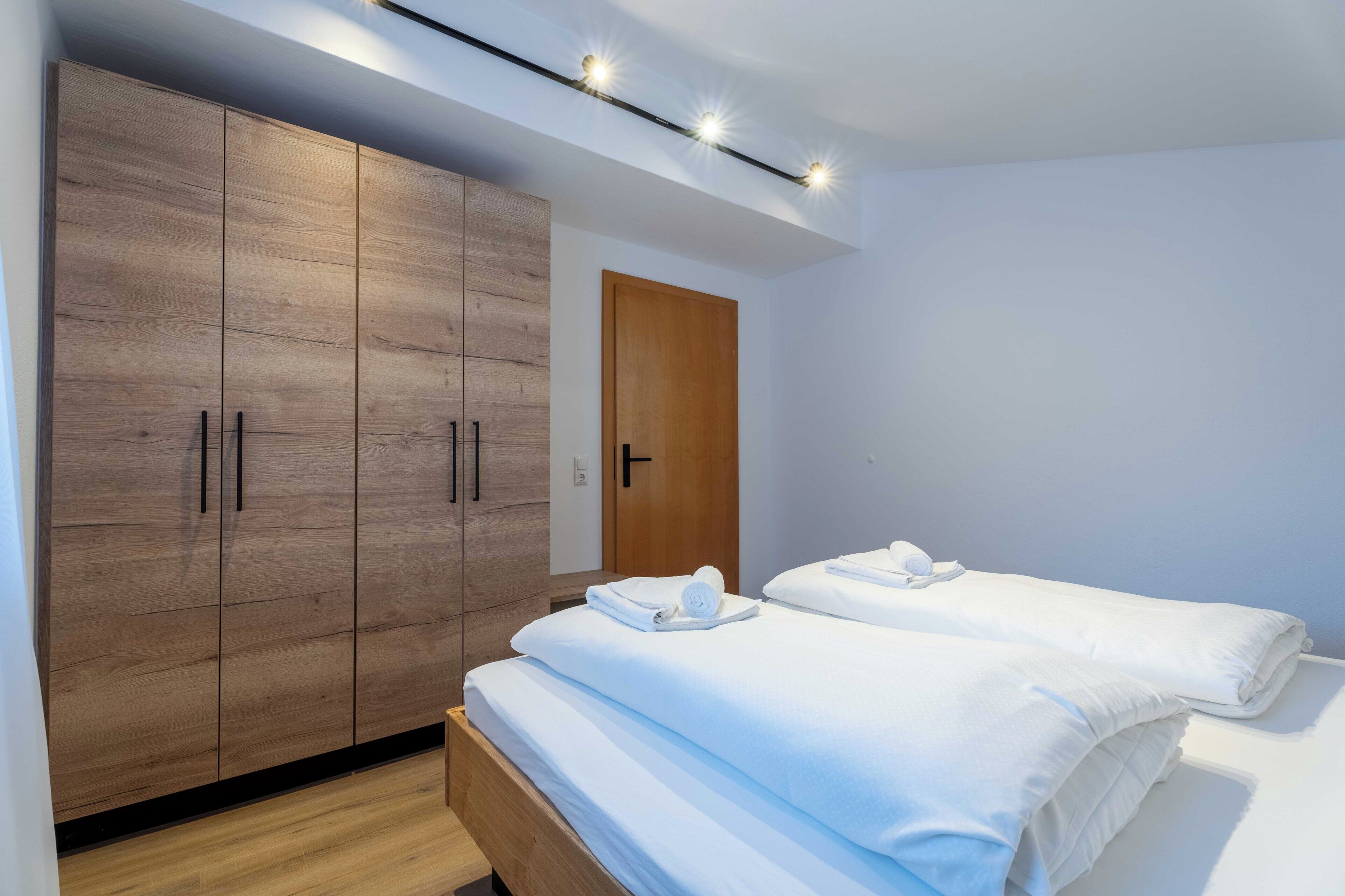 A modern bedroom with a wooden wardrobe, two beds, and a ceiling light fixture.