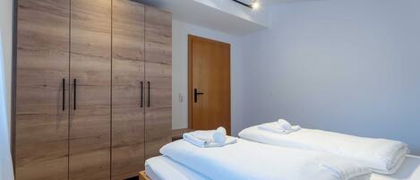 A modern bedroom with a wooden wardrobe, two beds, and a ceiling light fixture.