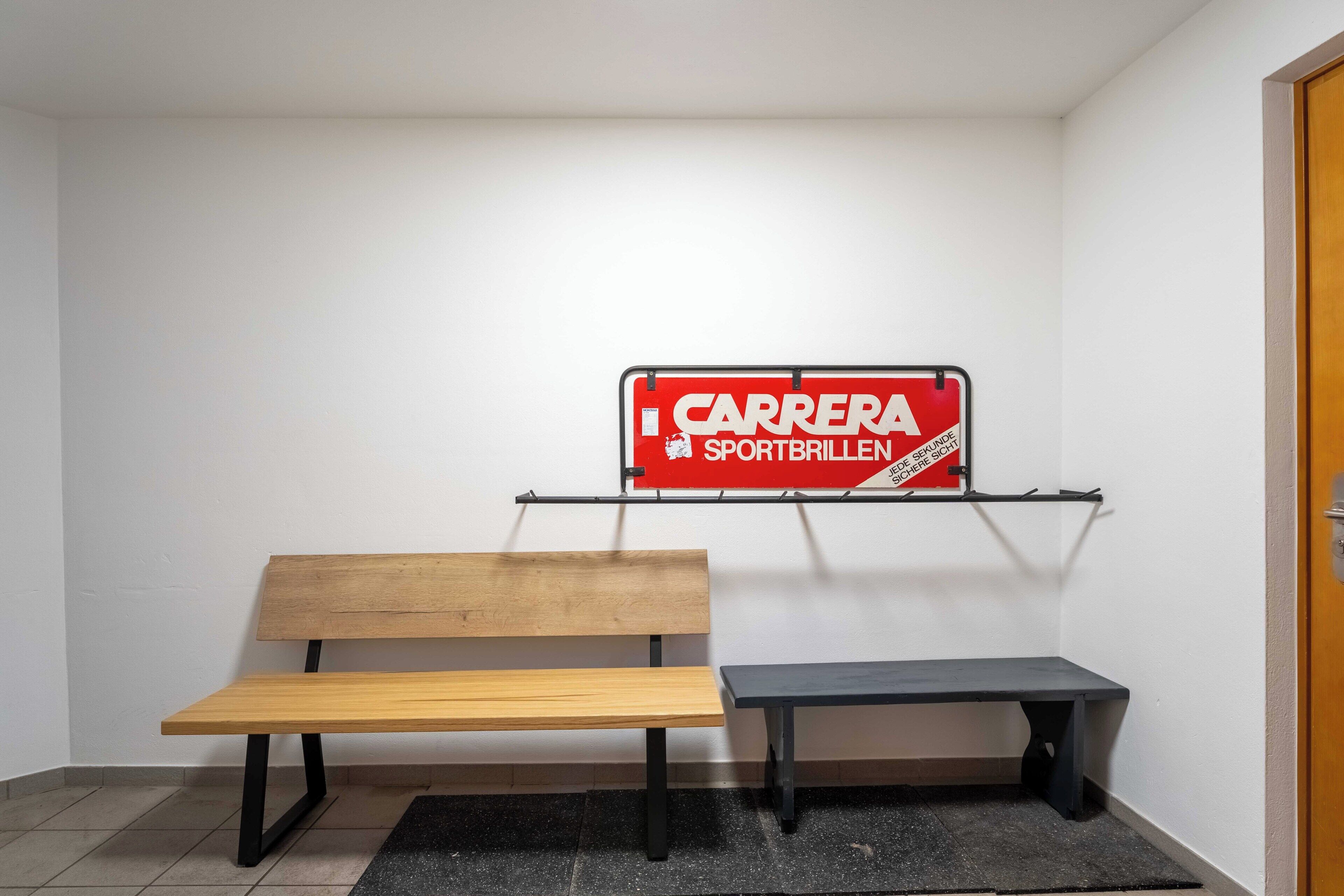 Une pièce avec un banc en bois, un banc noir et un panneau rouge accroché au mur.