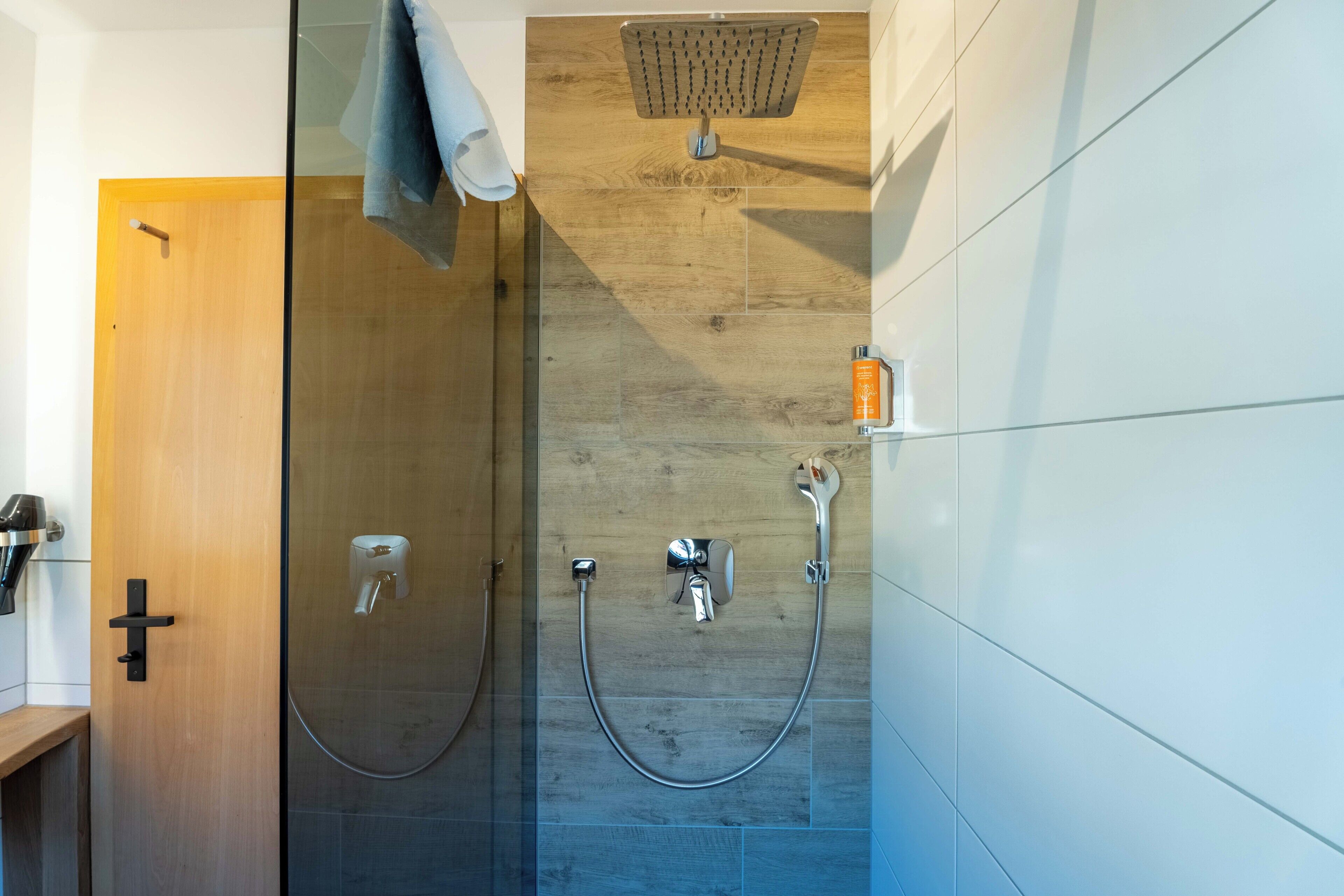 A modern bathroom with a glass shower enclosure, a wooden wall, and a white tiled wall.