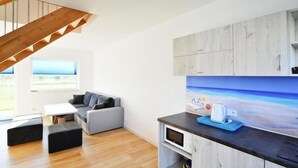 A modern living room with a wooden staircase, a grey sofa, a white table, and a kitchen area with a microwave and a coffee maker. - Comfortable holiday homes with a summer pool (Jaroslawiec)